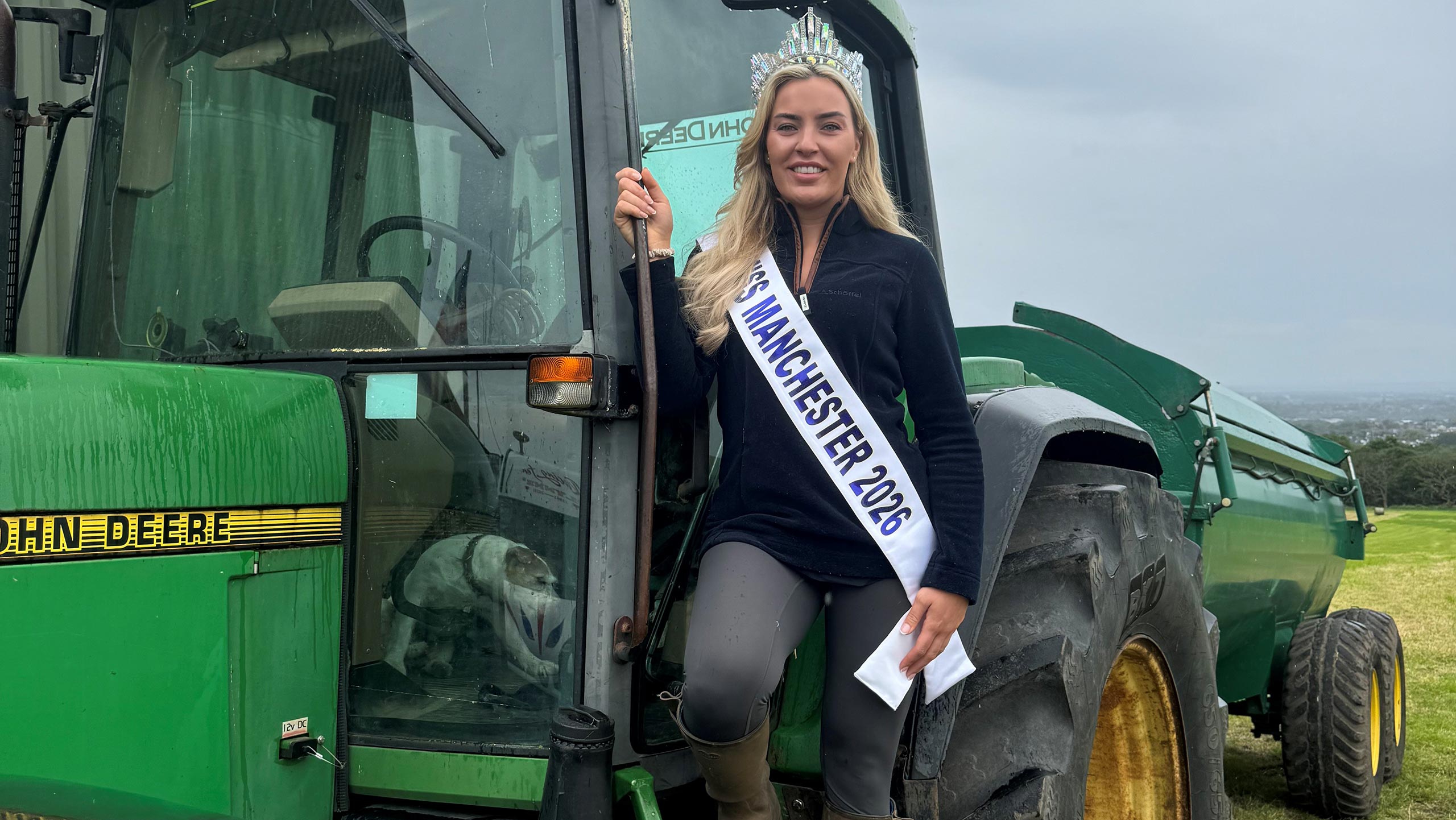 Clare beside a tractor wearing her Miss Manchester crown and sash